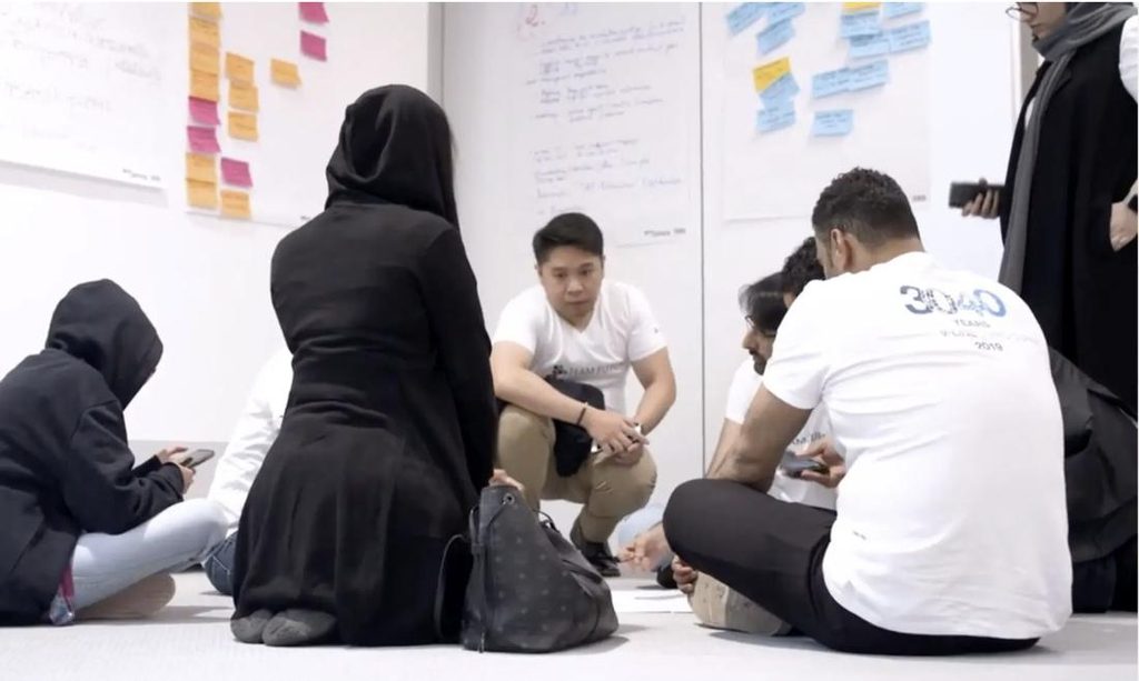 Vested team members sitting on the floor around sticky notes during a RealPlay workshop session